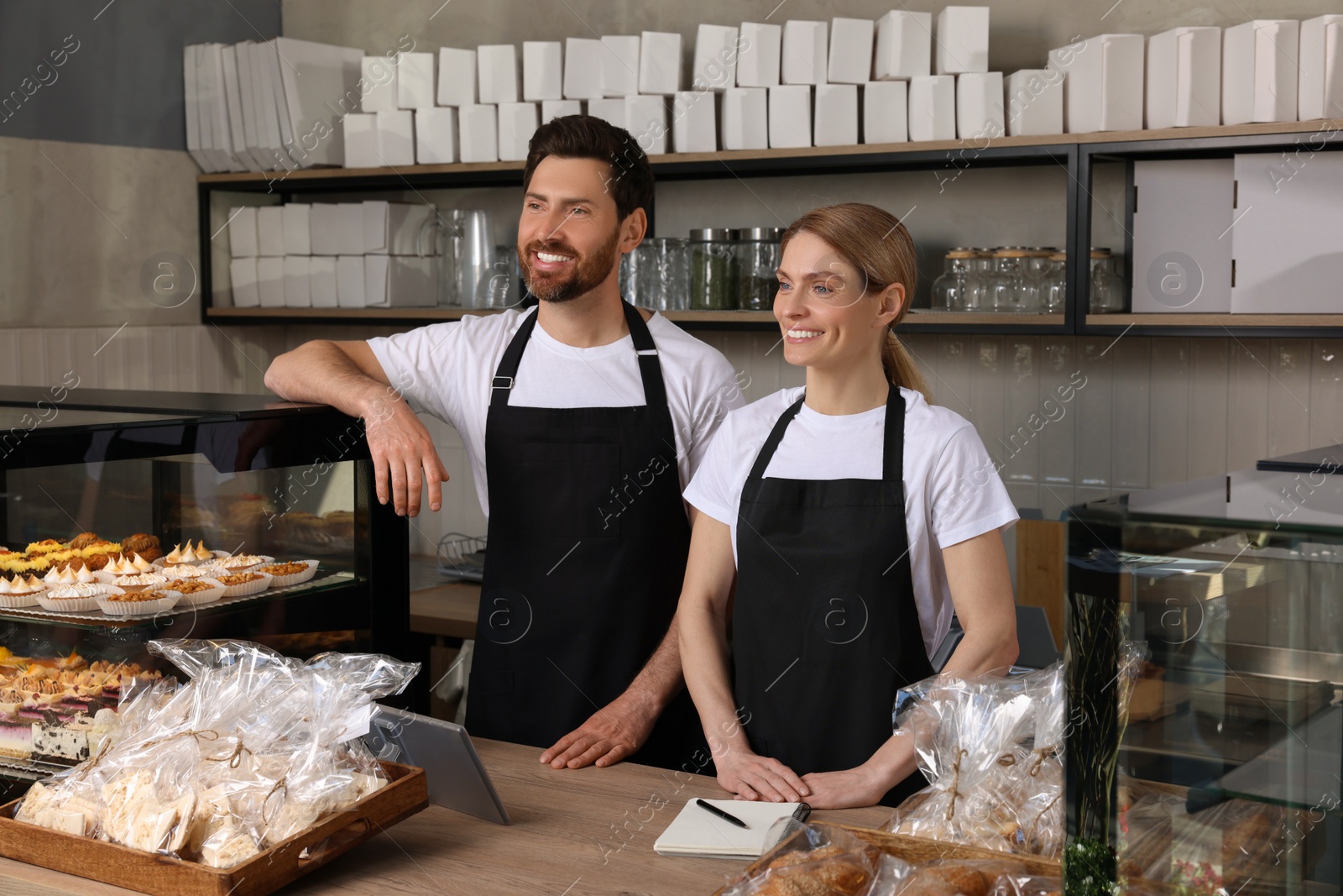 Photo of Happy sellers at cashier desk near showcase in bakery shop