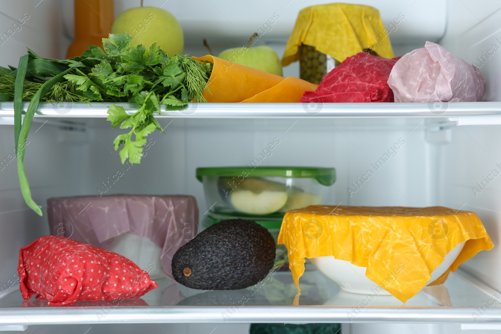 Photo of Open refrigerator with many different products packed in beeswax food wraps