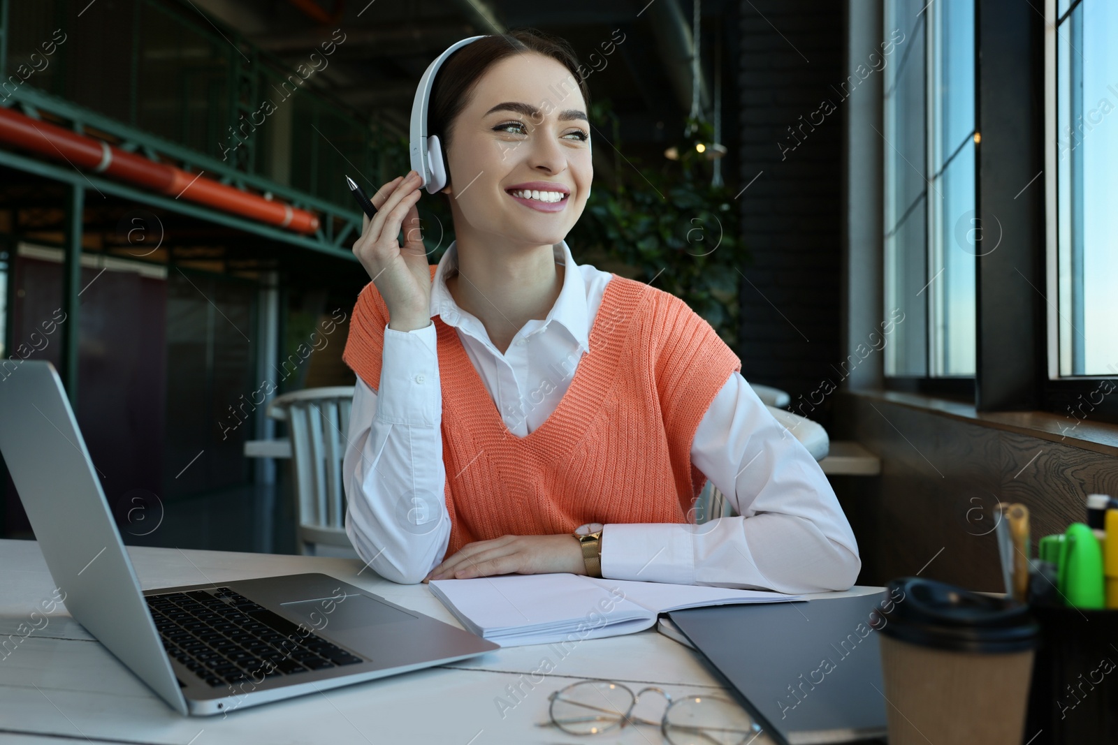 Photo of Young female student with laptop and headphones studying at table in cafe