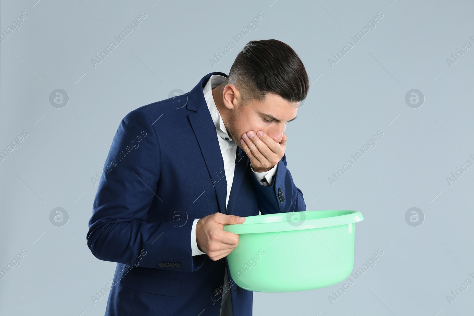 Photo of Man with basin suffering from nausea on grey background. Food poisoning