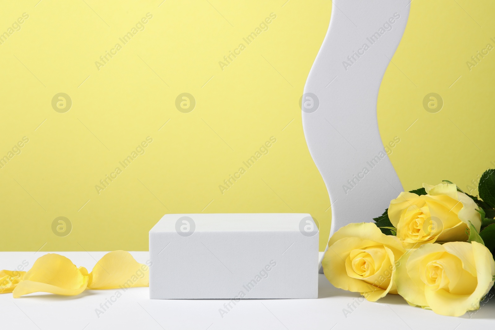 Photo of Beautiful presentation for product. Geometric figures and roses on white table against yellow background, space for text