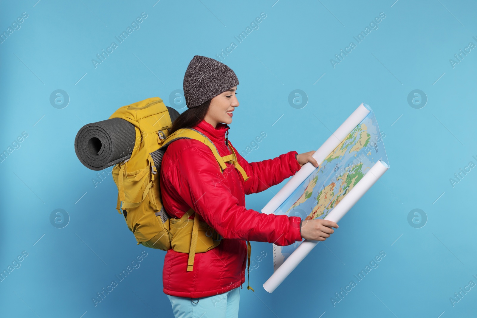 Photo of Smiling young woman with backpack and map on light blue background. Active tourism