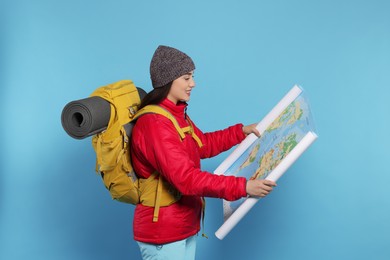 Photo of Smiling young woman with backpack and map on light blue background. Active tourism