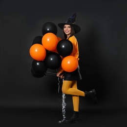 Photo of Beautiful woman wearing witch costume with balloons for Halloween party on black background, space for text