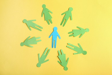 Photo of Circle of green paper human figures with blue one in middle on yellow background, flat lay. Diversity and inclusion concept