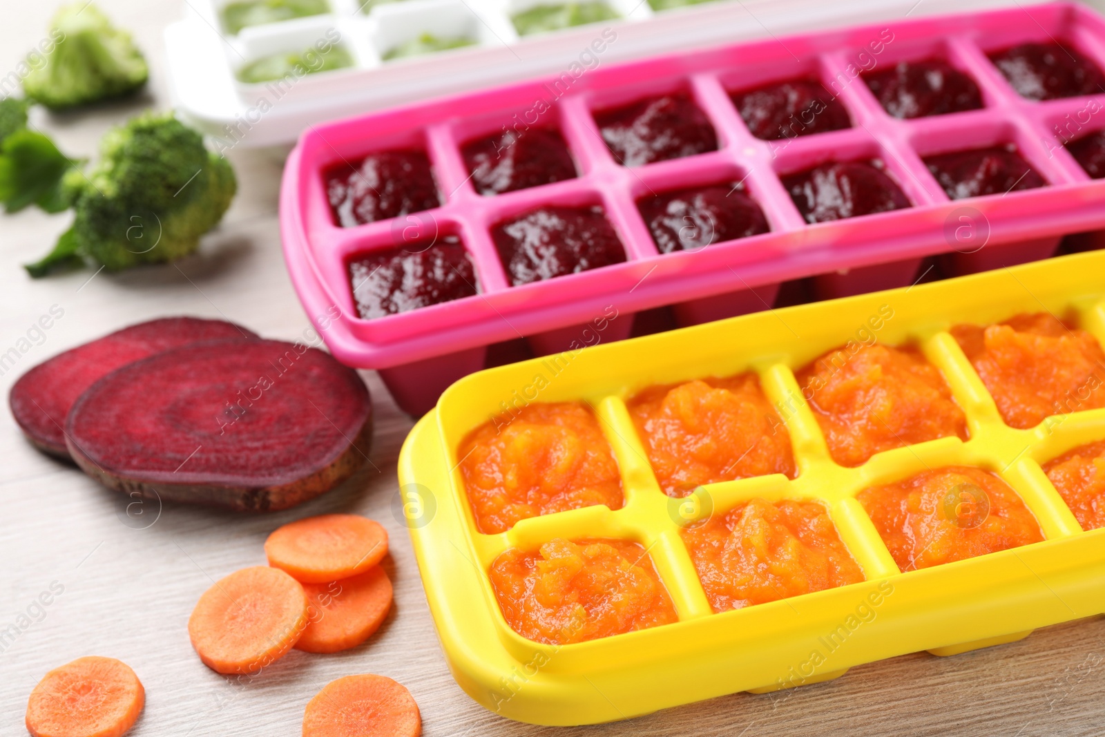 Photo of Different purees in ice cube trays and ingredients on white wooden table, closeup. Ready for freezing