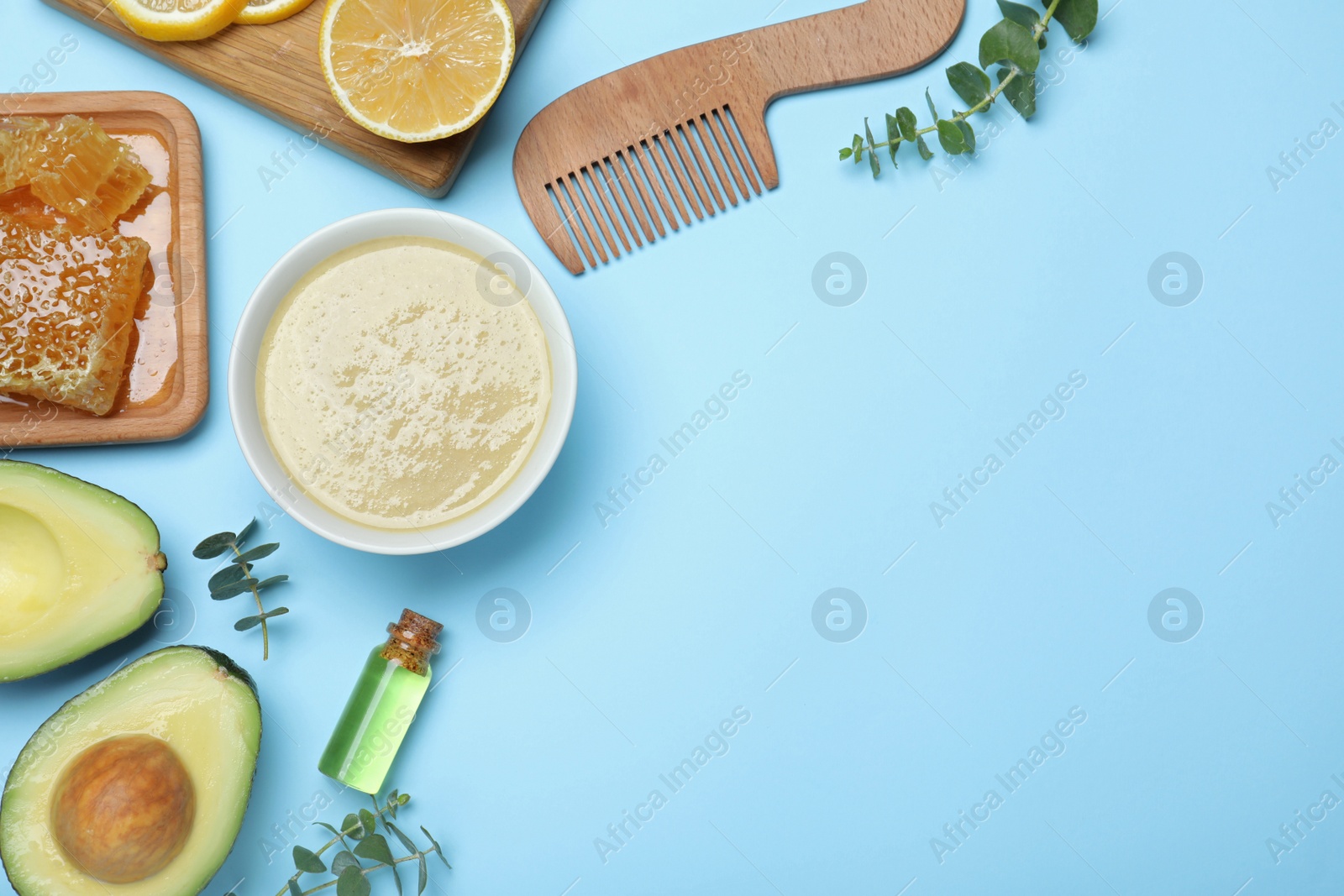 Photo of Homemade hair mask in bowl, fresh ingredients and bamboo comb on light blue background, flat lay. Space for text