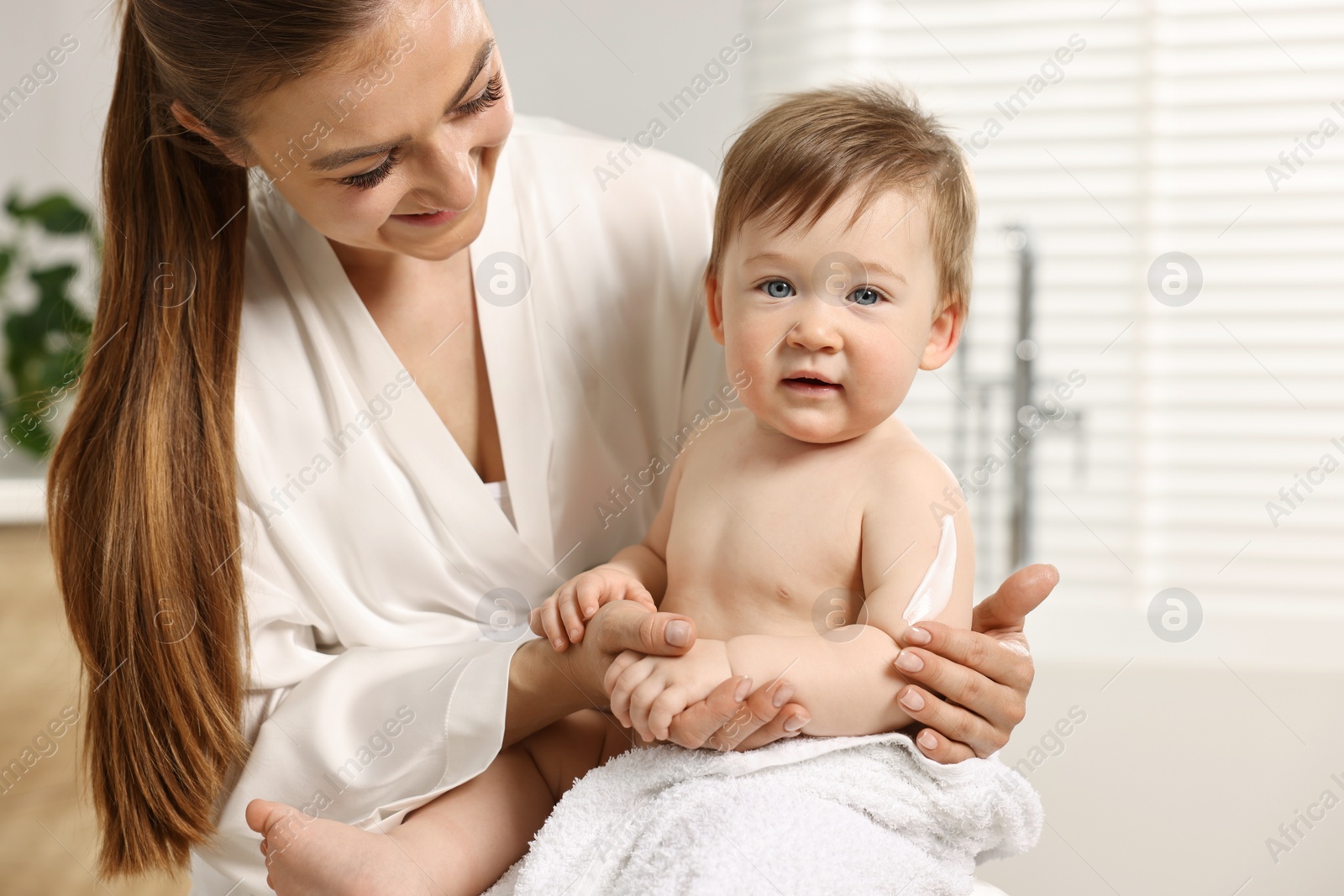 Photo of Happy mother applying body cream onto baby`s skin in bathroom