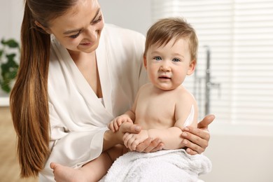 Photo of Happy mother applying body cream onto baby`s skin in bathroom