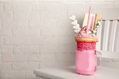 Tasty milk shake with sweets in mason jar on chair near brick wall. Space for text