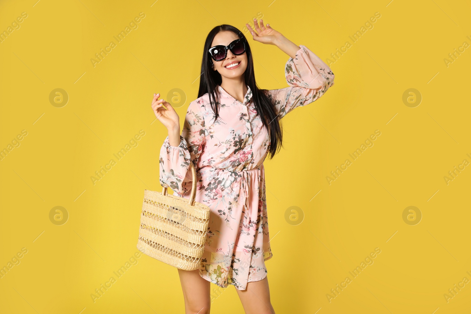 Photo of Young woman wearing floral print dress with straw bag on yellow background