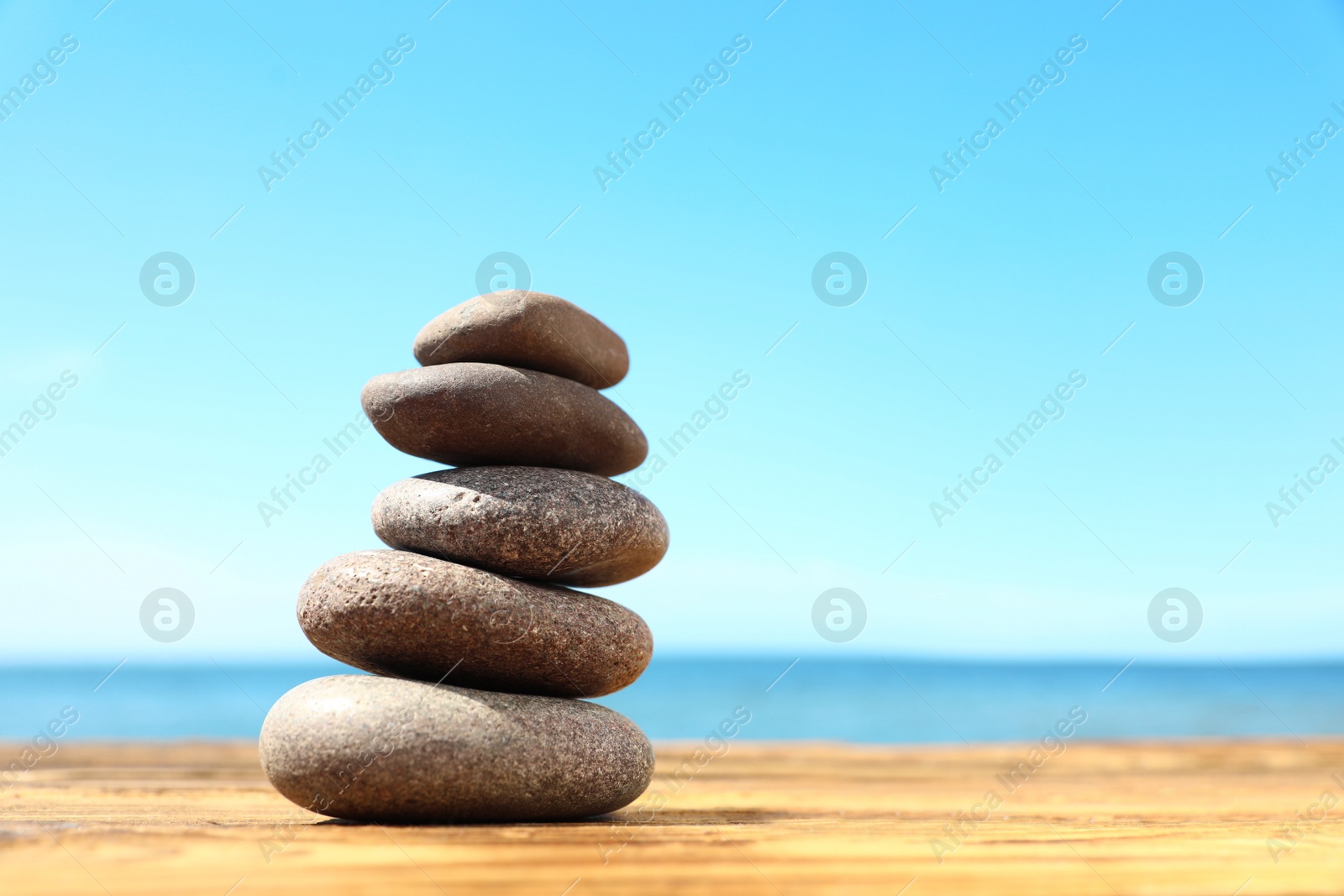 Photo of Stack of stones on wooden table against seascape, space for text. Zen concept