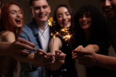 Happy friends with sparklers celebrating birthday indoors, focus on hands