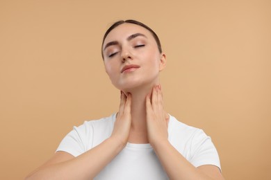 Beautiful woman touching her neck on beige background