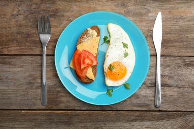 Photo of Fried sunny side up egg and sandwich served on wooden table, flat lay