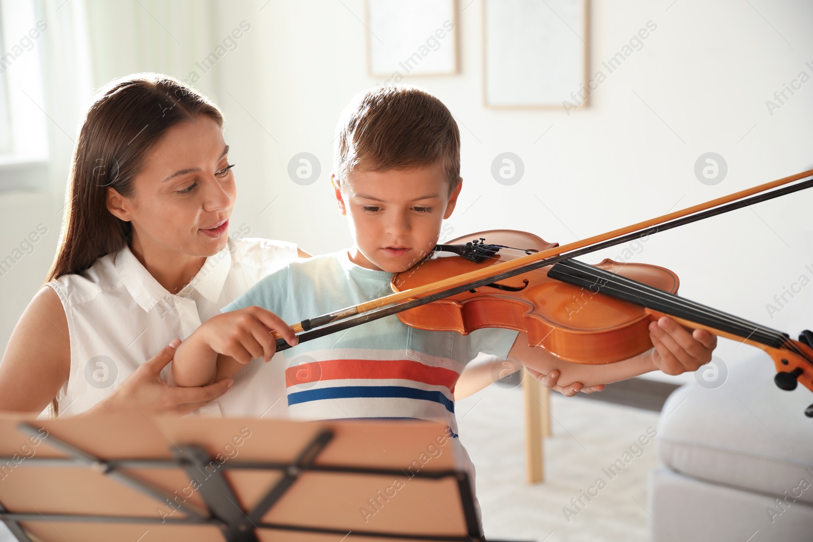 Photo of Young woman teaching little boy to play violin indoors