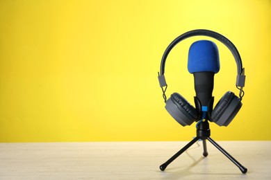 Photo of Microphone and modern headphones on white wooden table against yellow background, space for text