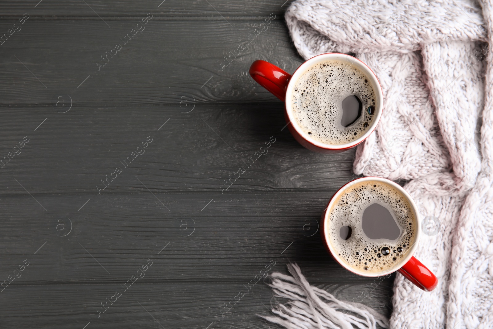 Photo of Flat lay composition cups of hot coffee and knitted scarf on grey wooden background, space for text. Winter drink