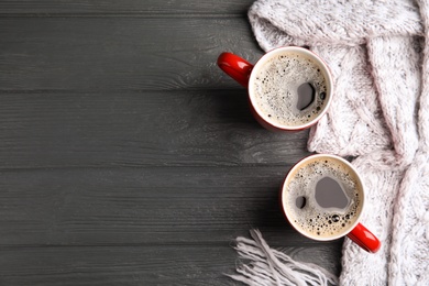 Photo of Flat lay composition cups of hot coffee and knitted scarf on grey wooden background, space for text. Winter drink