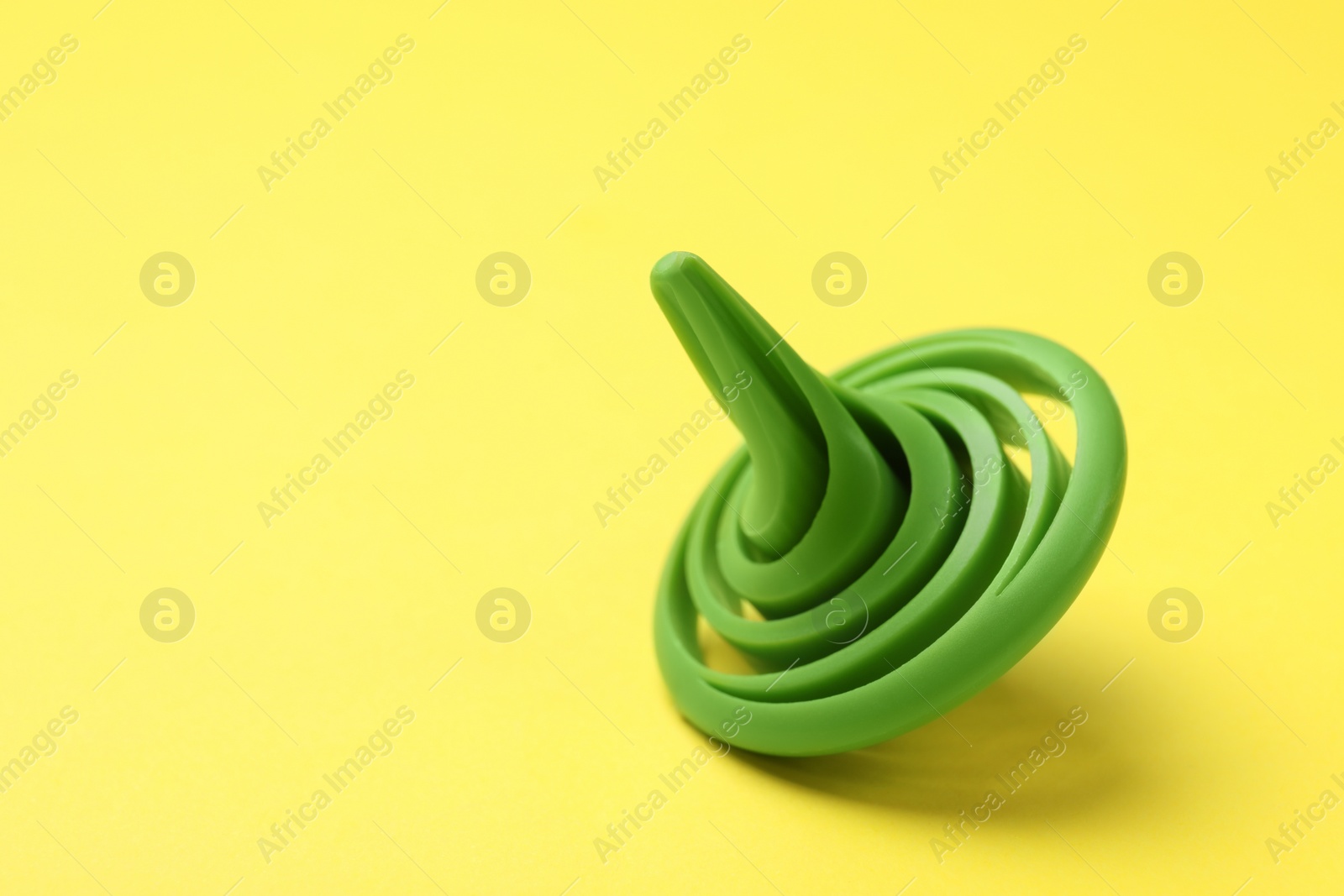 Photo of One green spinning top on yellow background, closeup. Space for text