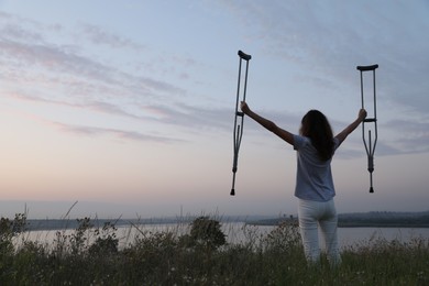 Woman holding axillary crutches outdoors at sunrise, back view. Healing miracle