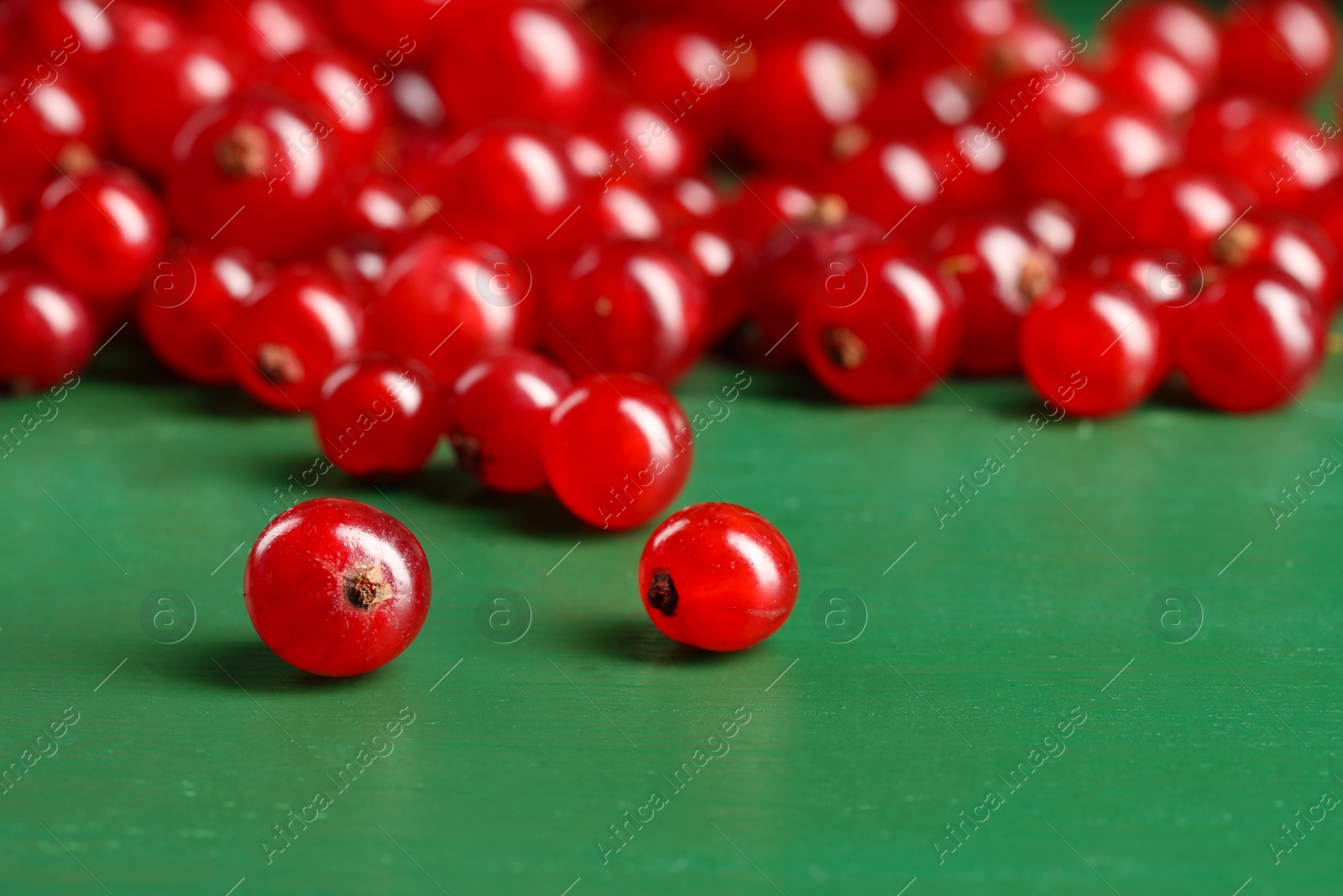 Photo of Many ripe red currants on green wooden table, closeup