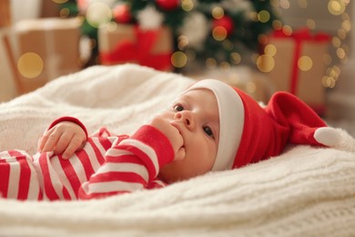 Photo of Cute little baby wearing Santa hat on blanket in room decorated for Christmas