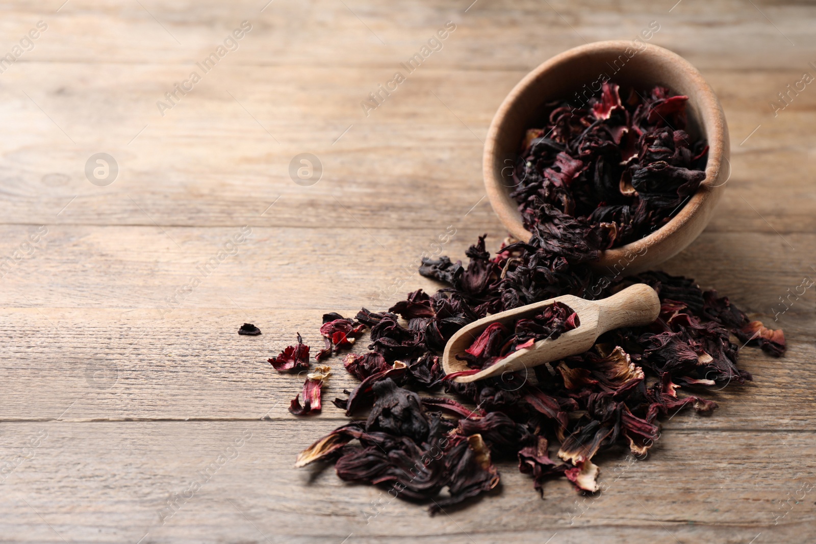 Photo of Scoop and bowl with dry hibiscus tea on wooden table. Space for text