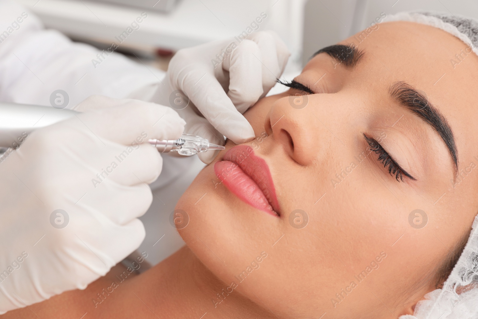 Photo of Young woman undergoing procedure of permanent lip makeup in tattoo salon, closeup