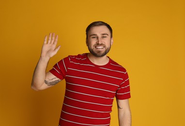 Photo of Happy young man waving to say hello on yellow background