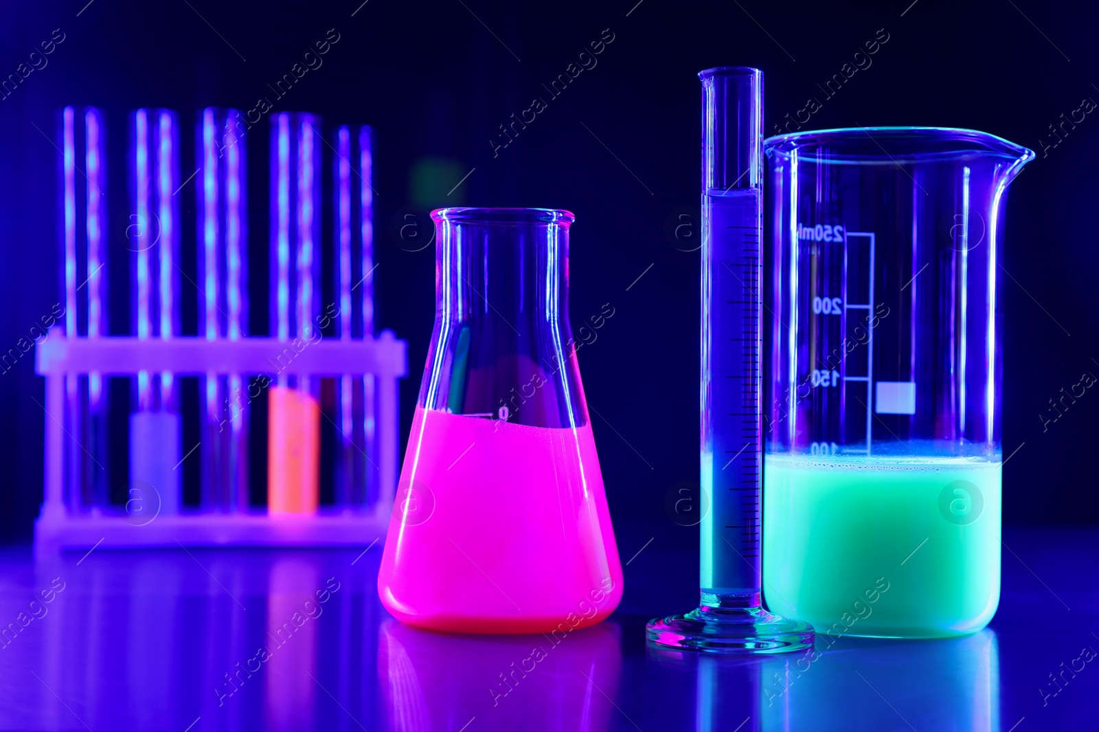 Photo of Laboratory glassware with luminous liquids on table against dark blue background