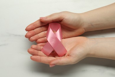 Photo of Woman with pink ribbon at white marble table, top view. Breast cancer awareness