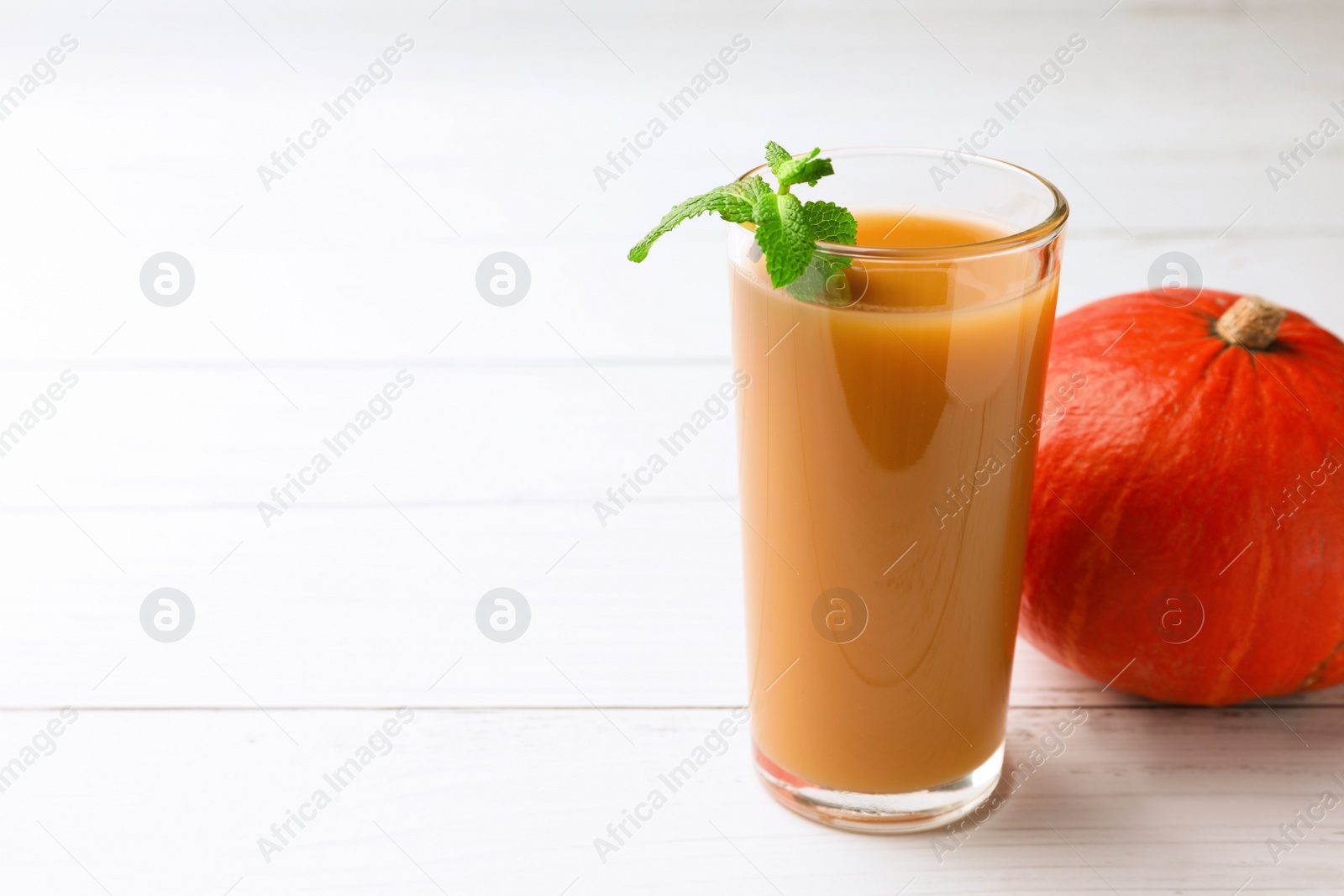 Photo of Tasty pumpkin juice in glass and whole pumpkin on white wooden table. Space for text