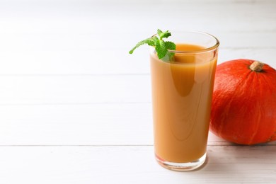 Photo of Tasty pumpkin juice in glass and whole pumpkin on white wooden table. Space for text