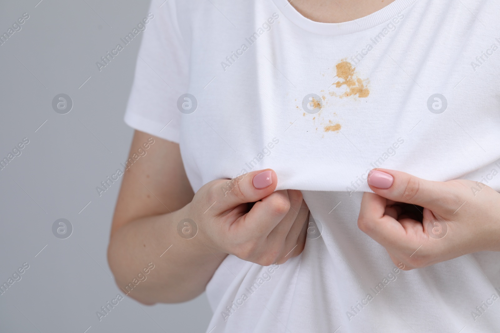 Photo of Woman showing stain on her t-shirt against light grey background, closeup