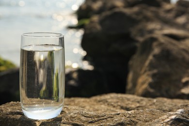 Photo of Glass of fresh water on stone near sea, space for text