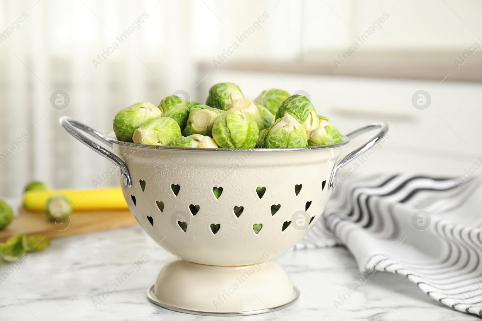 Photo of Colander with fresh Brussels sprouts on white marble table, closeup