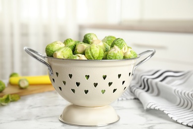 Colander with fresh Brussels sprouts on white marble table, closeup