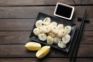 Photo of Raw scallops with green onion, soy sauce, lemon and chopsticks on wooden table, flat lay. Space for text