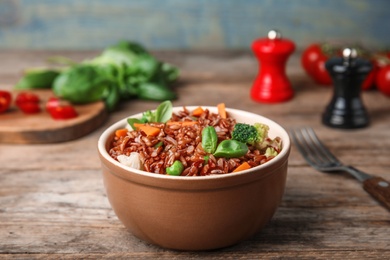 Photo of Bowl of brown rice with vegetables on wooden table