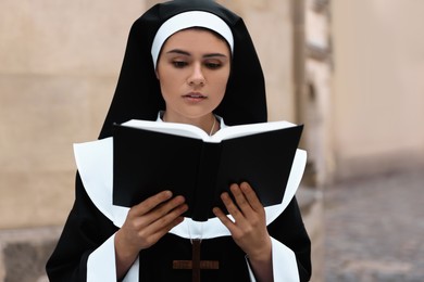 Photo of Young nun reading Bible near building outdoors