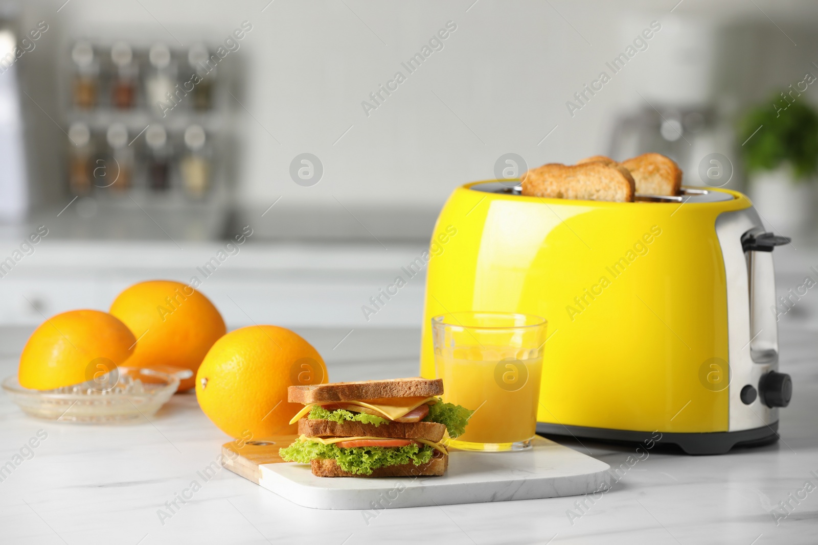 Photo of Yellow toaster with roasted bread slices, sandwich, oranges and juice on white marble table