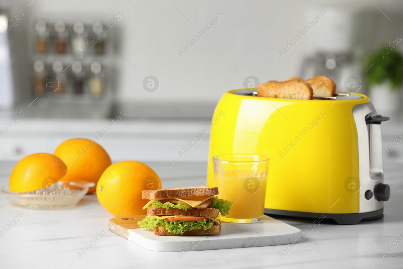 Yellow toaster with roasted bread slices, sandwich, oranges and juice on white marble table Photo of Yellow toaster with roasted bread slices, sandwich, oranges and juice on white marble table