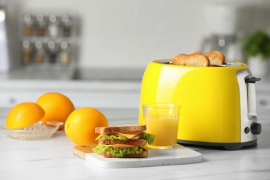 Photo of Yellow toaster with roasted bread slices, sandwich, oranges and juice on white marble table