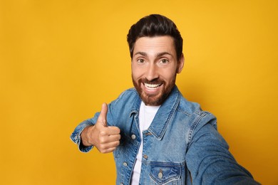 Photo of Handsome bearded man showing thumb up while taking selfie on orange background