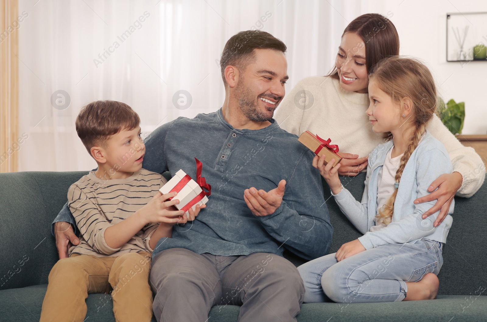 Photo of Happy family presenting each other with gifts on sofa at home