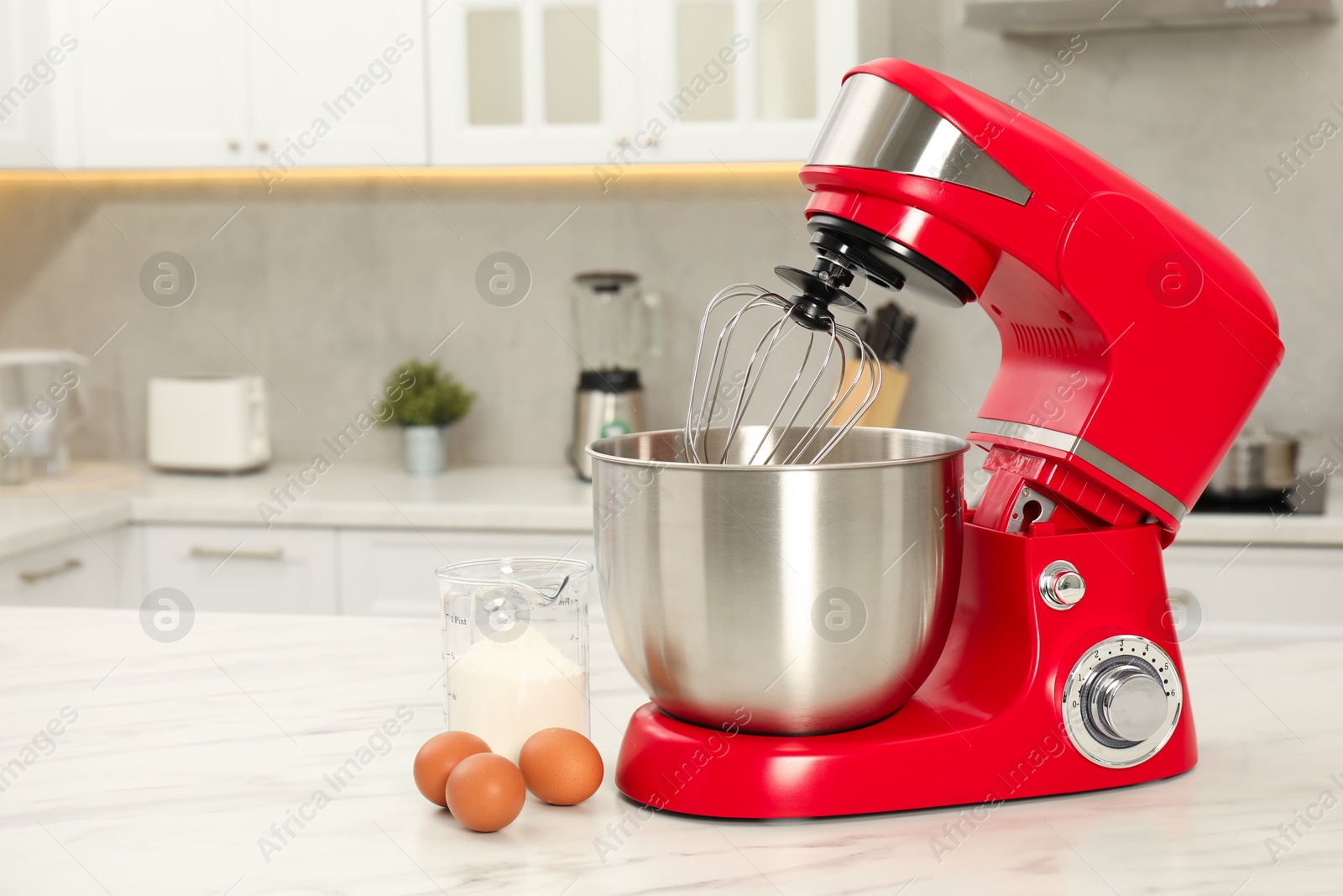 Photo of Modern red stand mixer, eggs and container with flour on white marble table in kitchen, space for text