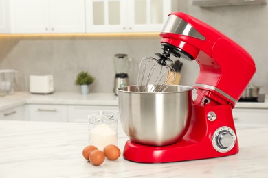 Photo of Modern red stand mixer, eggs and container with flour on white marble table in kitchen, space for text