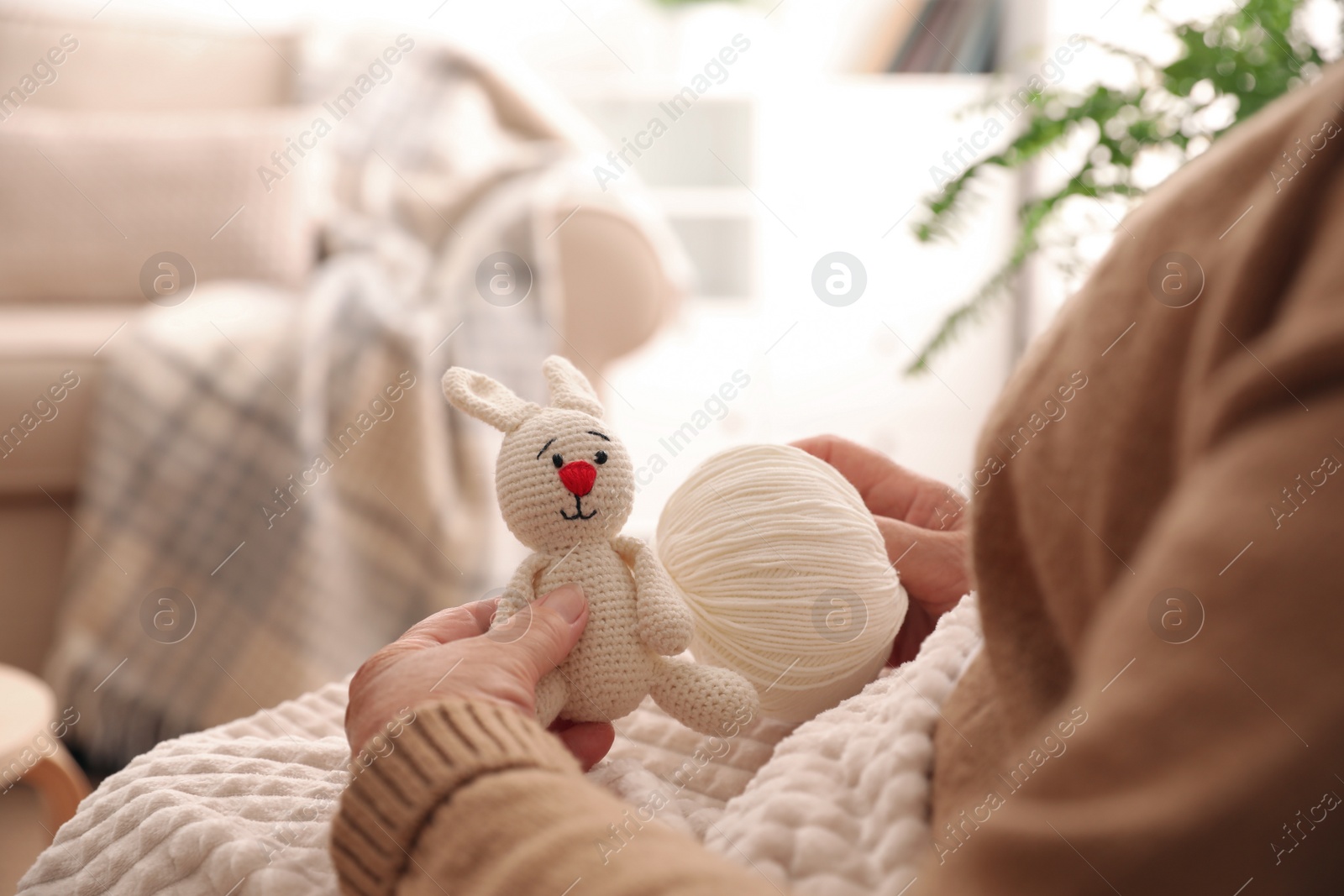 Photo of Elderly woman with knitted bunny at home, closeup. Creative hobby