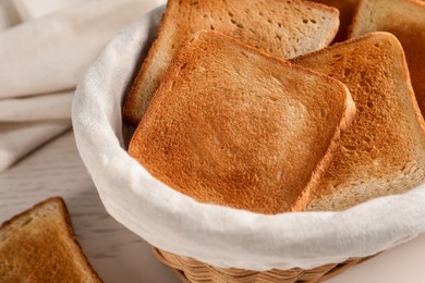 Photo of Wicker basket with slices of delicious toasted bread on white wooden table, closeup